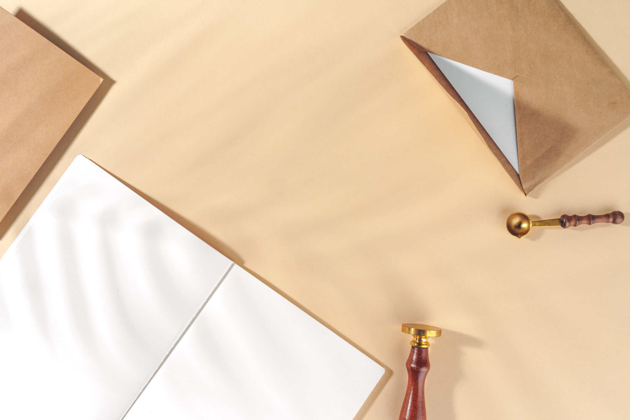 Wax seal stamp and sealing spoon arranged with envelopes an paper on a warm beige background.