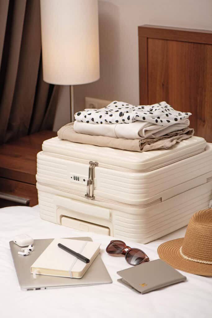 Packed suitcase with folded clothes, notebook, sunglasses, hat, and travel essentials laid out for a trip
