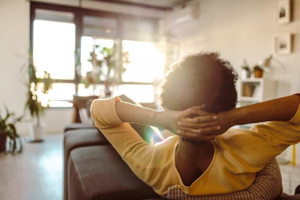 Why do I feel guilty doing nothing? Woman sitting quietly on couch, during downtime at home.