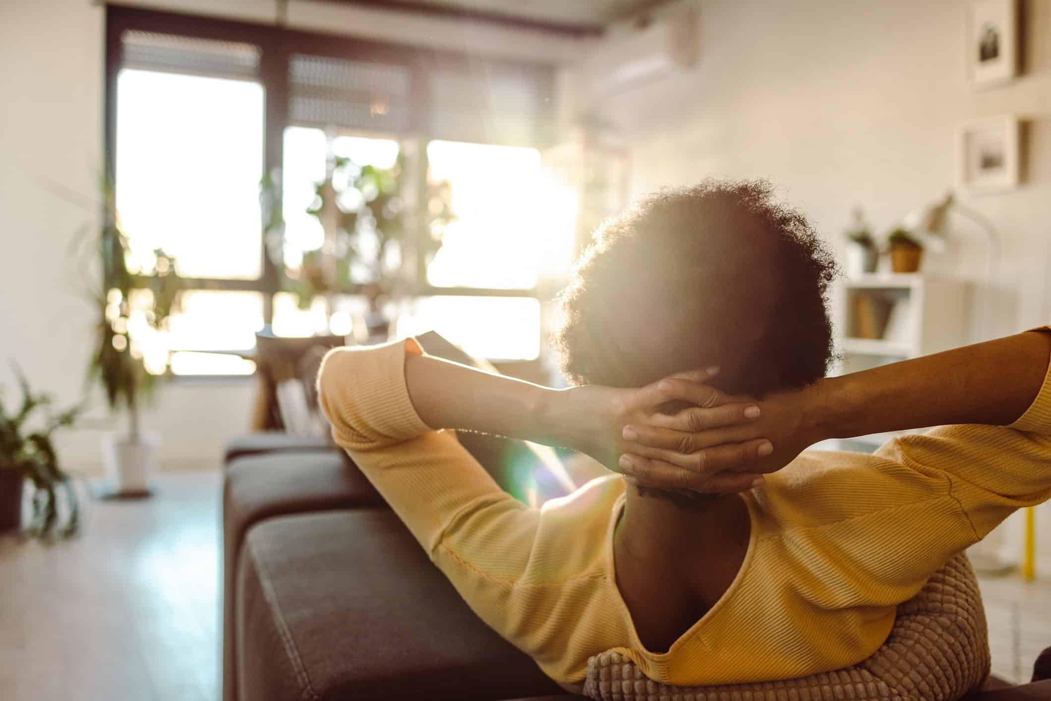 Why do I feel guilty doing nothing? Woman sitting quietly on couch, during downtime at home.